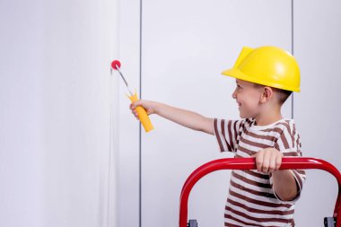 Boyalı silindirli şirin bir çocuk. Mutlu çocuk ebeveynlerin duvar boyamasına yardım eder. Aile için yeni bir ev