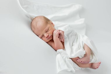Beyaz bir örtüye sarılmış, beyaz bir arka planda uyuyan 3 günlük bir bebek..