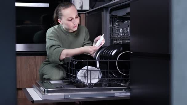 女性は食器洗い機から清潔な料理をアンロードします 喜びの宿題について — ストック動画