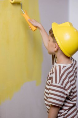 Boyalı silindirli şirin bir çocuk. Mutlu çocuk ebeveynlerin duvar boyamasına yardım eder. Aile için yeni bir ev