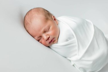 Beyaz bir örtüye sarılmış, beyaz bir arka planda uyuyan 3 günlük bir bebek..