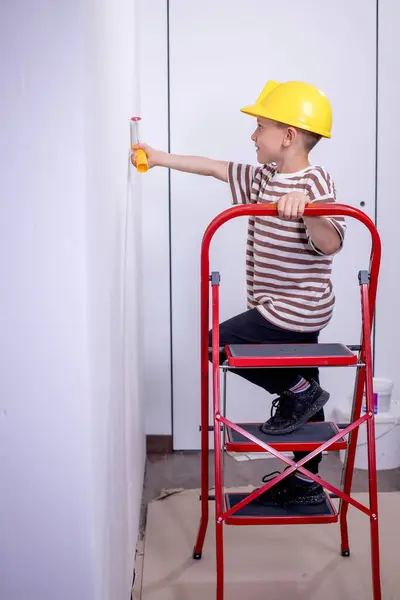 子供はローラーで壁を描いています その少年は大きなペンキブラシを持っている ハウス修理 ストック画像