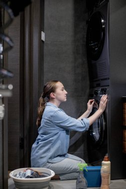 Kadın otomatik çamaşır makinesini açar ya da banyodaki kontrol paneli düğmeli programı, evdeki modern aletleri seçer..