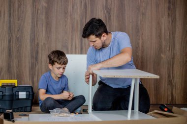 Baba ve oğul yeni dairenin zemininde yeni mobilyalar birleştiriyor. Tecrübe ve eğitim kavramı.