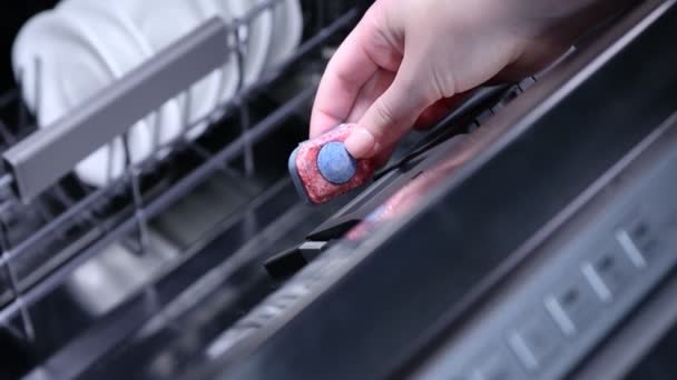 食器洗い機に青い洗剤カプセルを入れる女性の手のクローズアップ — ストック動画