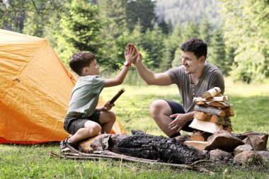 Oğlu ve babası mangalda mangal hazırlıyorlar. Terbiye edilmiş et kömürde kızartılır. Çadırın yanında barbekü hazırlama süreci