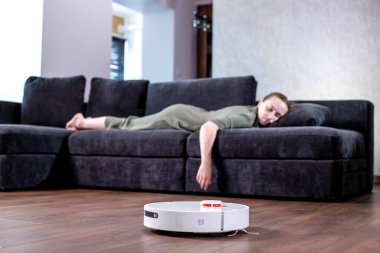 Kadın kanepede dinlenirken robot süpürgesi odayı temizliyor..