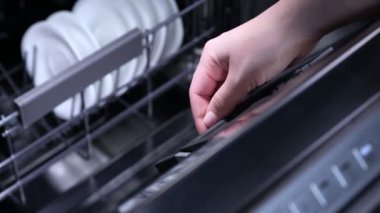 Bulaşık makinesine mavi deterjan koyan kadının eli yakın plan.