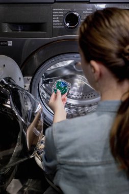 Çamaşır deterjanı kapsülünü çamaşır makinesine koyan kadın, yakın plan. Çamaşır yıkama. Yıkama ve temizlik kavramı..