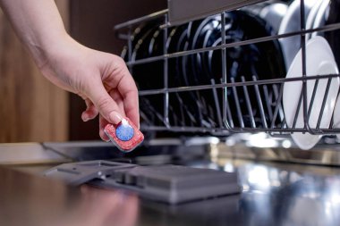 Açık bir bulaşık makinesinin arka planına karşı bir kadının ellerinde bulaşık makinesi tableti..