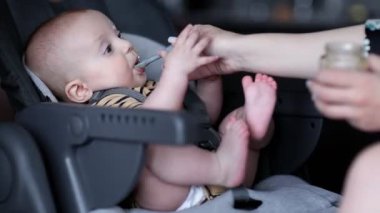Anne oğlunu yüksek sandalyede besliyor. Bebeğin ilk tamamlayıcı yiyeceği..
