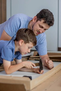 Oğlu, babasının mobilya toplamasına yardım ediyor. Yakınlarda da alet ve tahtalar var. Evde mobilya montajı.