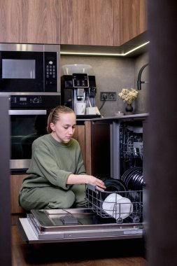 Kadın bulaşık makinesinden temiz bulaşıkları boşaltıyor..