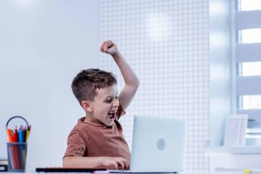 Neşeli okul çocuğu dizüstü bilgisayarla oturur ve başarıyı kutlar..