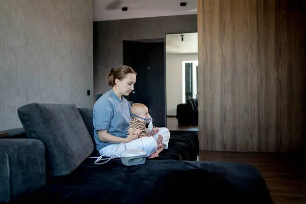 stock image Woman with infant son makes inhalations using a nebulizer at home.