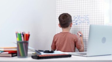 Beyaz tahtada matematik problemleri çözen genç bir çocuğun arka görünüşü.
