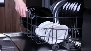 Kadın bulaşık makinesinin kapısını açtı ve temiz siyah beyaz çanak çömlek setiyle alt çekmeceyi çıkardı..