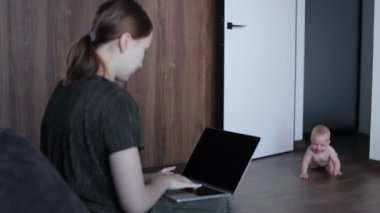 Sevimli küçük erkek bebek, annesinin kanepesinde oturuyor ve internette çalışıyor. Kadın serbest doğum izni alırken para kazanıyor..