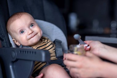 Mother feeding her son in a high chair. Baby's first complementary food. clipart