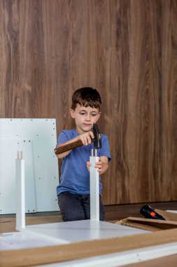 Oğlan çekiçle tahta bir çukur kazıyor. Evde mobilya montajı.