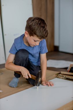 Oğlan çekiçle tahta bir çukur kazıyor. Evde mobilya montajı.