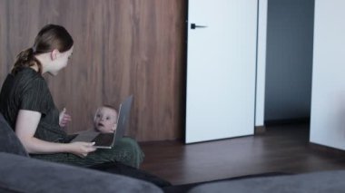 Sevimli küçük erkek bebek, annesinin kanepesinde oturuyor ve internette çalışıyor. Kadın serbest doğum izni alırken para kazanıyor.