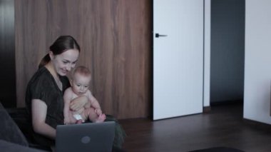Sevimli küçük erkek bebek, annesinin kanepesinde oturuyor ve internette çalışıyor. Kadın serbest doğum izni alırken para kazanıyor..