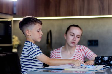 Anne, oğluna mutfakta ödev yaparken yardım ediyor..