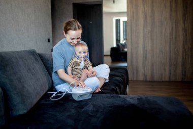 Küçük oğlu olan bir kadın evde nebulizör kullanarak solunum yapıyor..