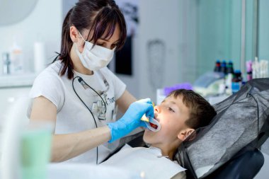 Çocuk dişçisi, diş tedavisinden önce çocuk hastaya yanak retraktörü takıyor..