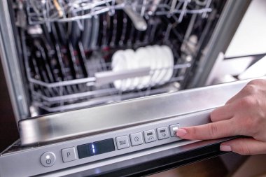 Bulaşıkları yıkamak için kadının eli bulaşık makinesini açıyor. Mutfakta ev aletleri var.