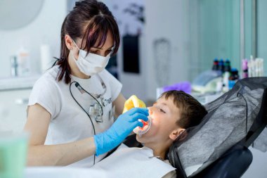 Çocuk dişçisi, diş tedavisinden önce çocuk hastaya yanak retraktörü takıyor..