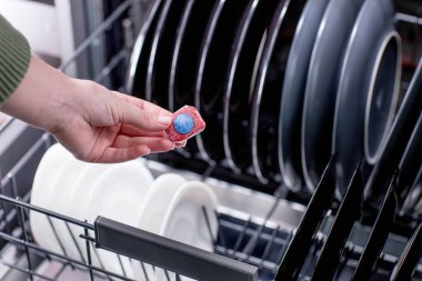 Açık bir bulaşık makinesinin arka planına karşı bir kadının ellerinde bulaşık makinesi tableti..