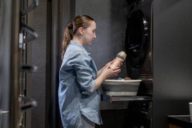 Genç bir kadın banyodaki giysiler için granüllerde saç kremi tutuyor.