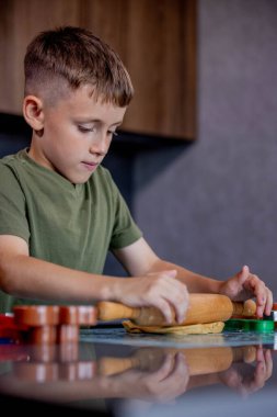 Küçük çocuk masaya merdaneyle zencefilli ekmek hamuru yuvarlıyor.