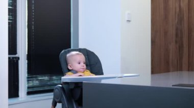 Bir yaşındaki bir çocuk mutfakta yüksek bir sandalyede otururken abur cubur yer..