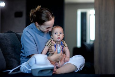 Bir kadın çocuğunun yüzüne nebulizör maskesi takıyor..