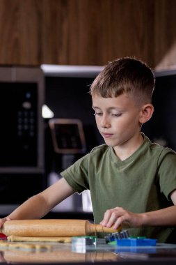 Küçük çocuk masaya merdaneyle zencefilli ekmek hamuru yuvarlıyor.