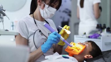Bir çocuk diş kliniğinde bakıcılık yapıyor. Bir çocuğun hastalıklı dişini dolduran modern fotopolimer yerleştirme süreci.