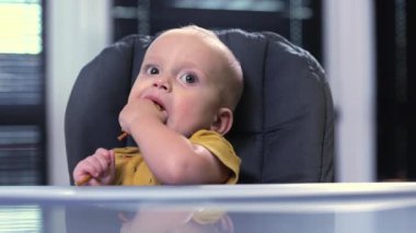 Bir yaşındaki bir çocuk mutfakta yüksek bir sandalyede otururken abur cubur yer..