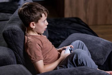 Oğlan evdeki kanepede oturup oyun oynuyor.