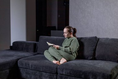 Güzel genç bayan rahat bir kanepede oturup kitap okuyor..