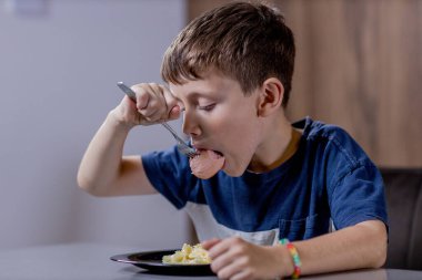 Küçük çocuk mutlu mesut sosisli makarna yiyor..