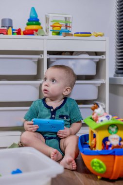 Küçük bir bebek rengarenk bir oyuncak telefonla oynarken yerde mutlu bir şekilde oturuyor ve oyun zamanının tadını çıkarıyor.