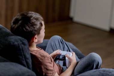 Oğlan evdeki kanepede oturup oyun oynuyor.