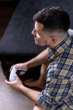 Bir adam elinde bir video oyun kumandası tutarken koltukta rahatça oturur ve oynadığı oyuna dalmıştır.