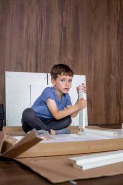 Giyinen genç bir çocuk özenle mobilya topluyor, işine odaklanıyor ve özen gösteriyor..