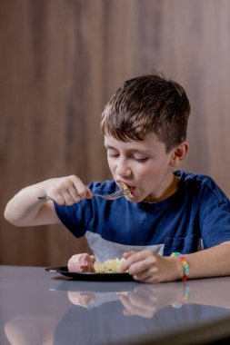 Küçük çocuk mutlu mesut sosisli makarna yiyor..