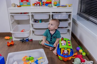 Küçük bir bebek rengarenk bir oyuncak telefonla oynarken yerde mutlu bir şekilde oturuyor ve oyun zamanının tadını çıkarıyor.