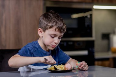Küçük çocuk mutlu mesut sosisli makarna yiyor..